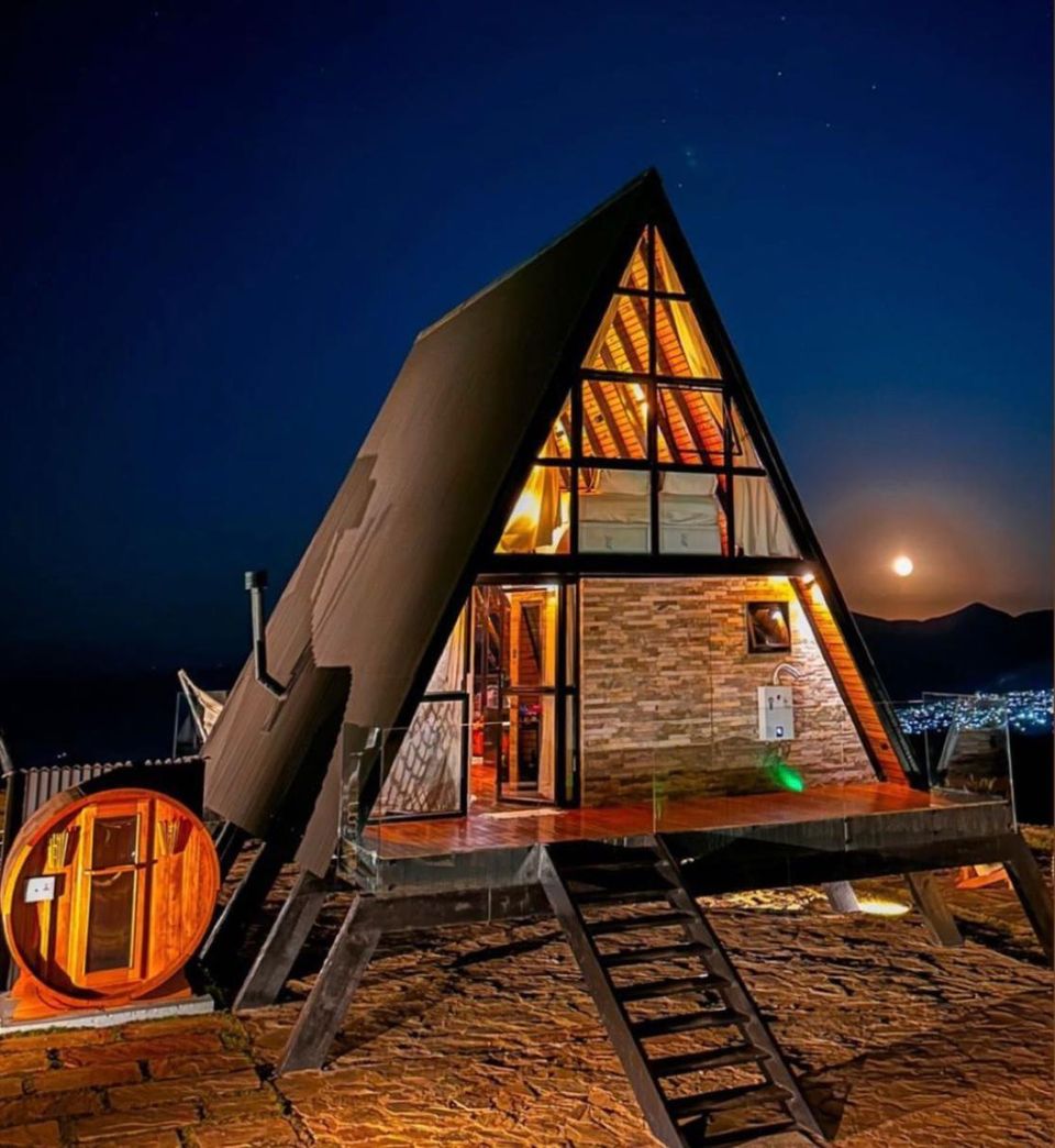 Chalé Personalité iluminado à noite, com dois andares, sauna barril e lua sobre as montanhas