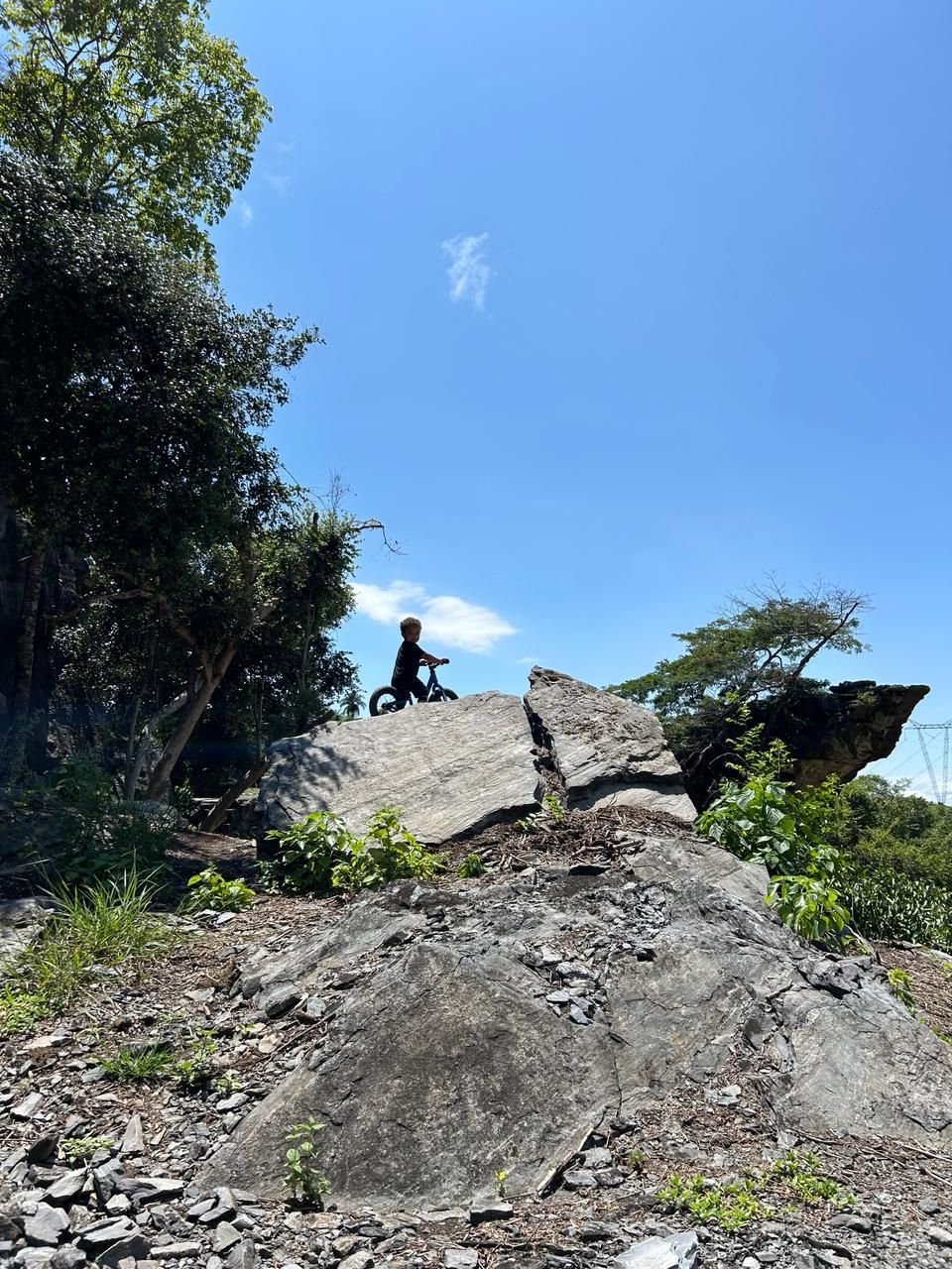 Criança com bicicleta no alto de uma grande pedra sob o céu azul