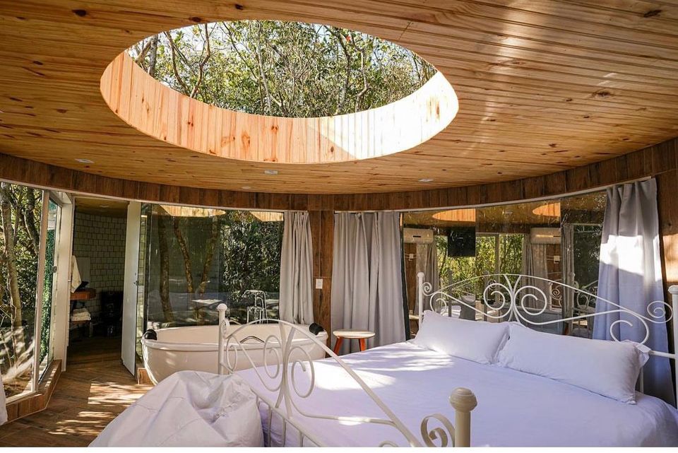 Interior de chalé com teto de vidro circular, cama de casal e banheira