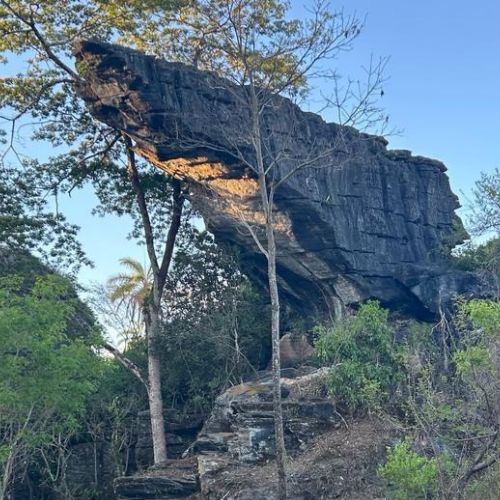 Grande lapa de pedra suspensa sobre a mata ao entardecer